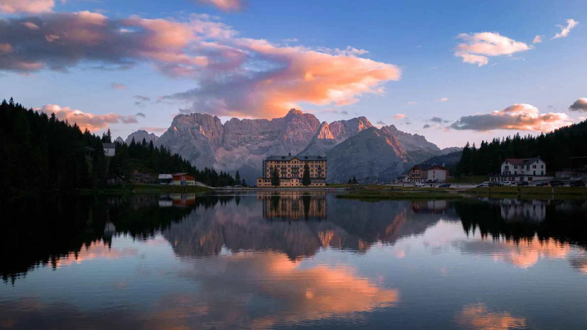 Lake Misurina mirroring pink sunset clouds and the peaks behind the lakeside hotel
