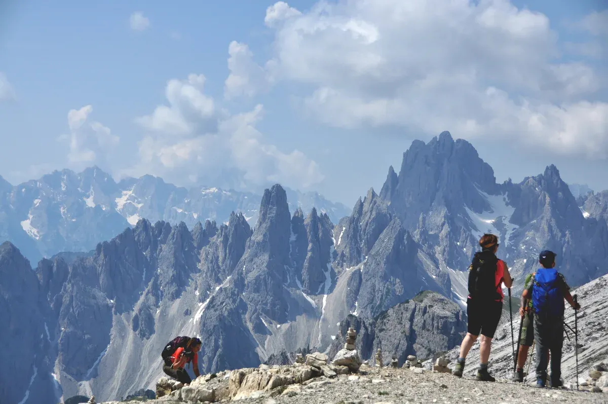 Two hikers with trekking poles and jackets looking over the Dolomites peaks, what to wear in the Dolomites on a mountain trail