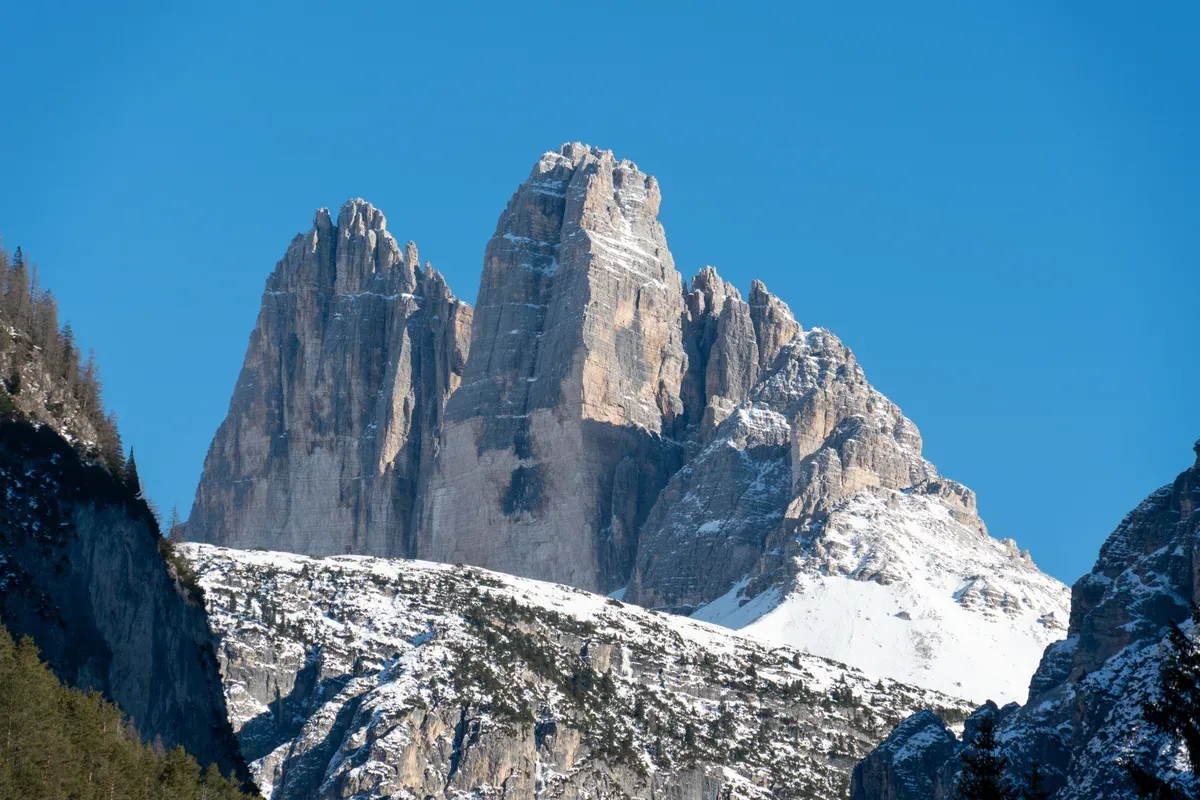 Tre Cime di Lavaredo above snow-covered scree slopes under a clear blue winter sky, the Dolomites in winter